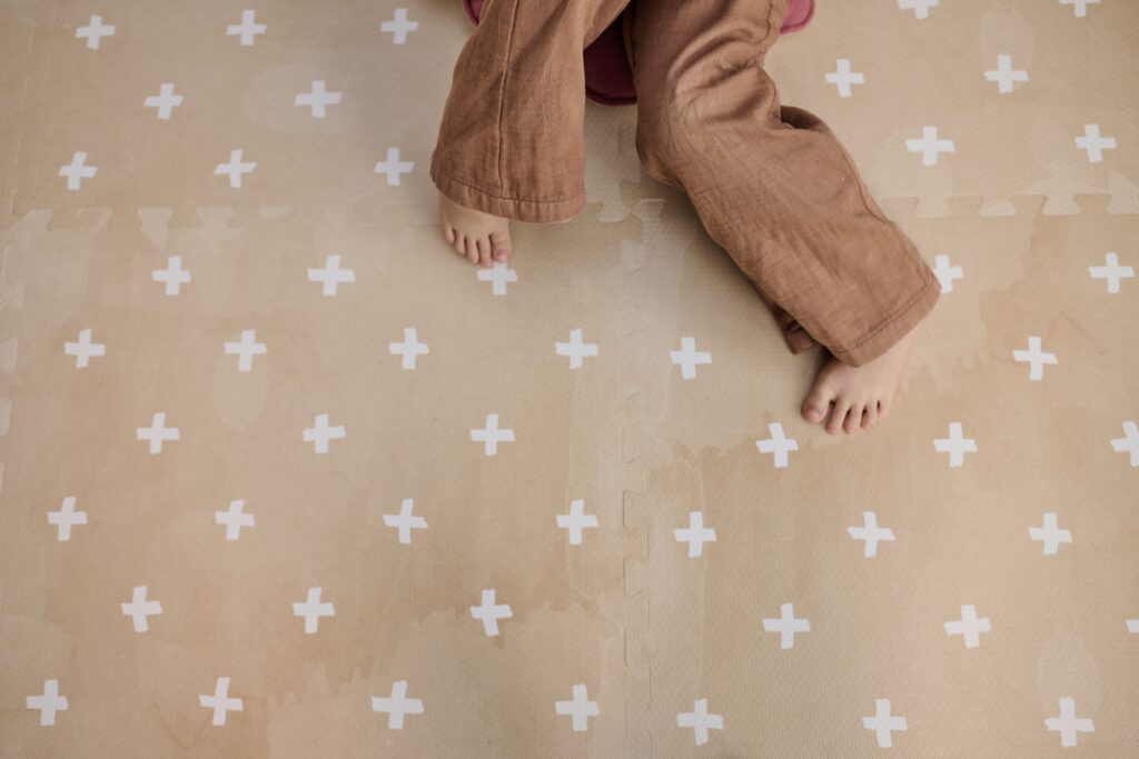 Dziecko na beżowej macie piankowej puzzle z białymi wzorami krzyżyków