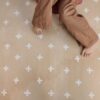Dziecko na beżowej macie piankowej puzzle z białymi wzorami krzyżyków